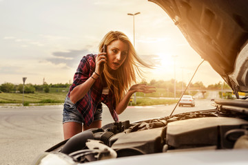 Attractive blonde in front of her car broken down car, assistance concept. Upset woman emotionally reacting on overheated car standing on the roadside with the open hood.