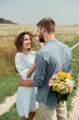 © LIGHTFIELD STUDIOS - man hiding bouquet of wild flowers for smiling girlfriend behind back in summer field