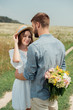 © LIGHTFIELD STUDIOS - man hiding bouquet of wild flowers for girlfriend behind back in summer field