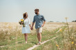 © LIGHTFIELD STUDIOS - smiling woman in white dress with bouquet of wild flowers walking together with boyfriend in field