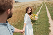 © LIGHTFIELD STUDIOS - partial view of smiling woman with bouquet of wild flowers and boyfriend holding hands in field