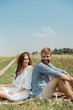 © LIGHTFIELD STUDIOS - young couple resting back to back on blanket in field with wild flowers on summer day