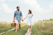 © LIGHTFIELD STUDIOS - smiling couple with picnic basket holding hands while walking in field