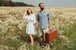 © LIGHTFIELD STUDIOS - happy couple with retro suitcase holding hands while standing in field with wild flowers