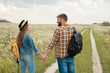© LIGHTFIELD STUDIOS - rear view of happy lovers with backpacks holding hands in field with wild flowers