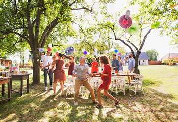 A senior couple and family dancing on a garden party outside in the backyard.