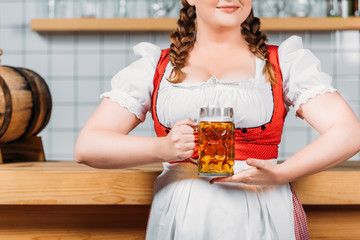 Wall Mural - cropped imageo of oktoberfest bartender in traditional bavarian dress holding mug of light beer near bar counter