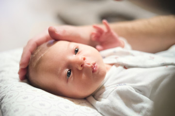 newborn baby lying on bed, unrecognizable father stroking her head.