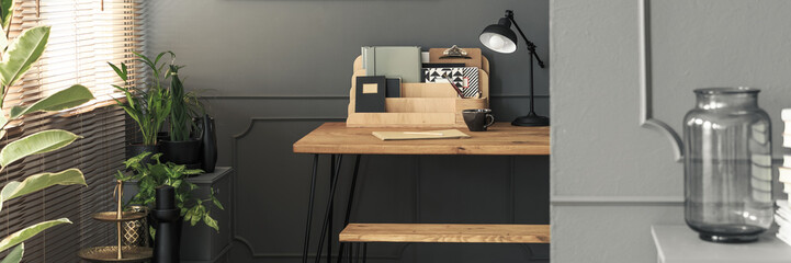 Organized folders and notebooks on a wooden desk with a black, industrial lamp - a creative study space in a gray, fancy apartment interior with plants