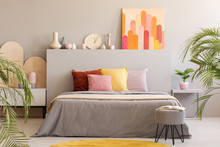 Painting On Grey Headboard Of Bed With Colorful Cushions In Bedroom Interior With Stool. Real Photo