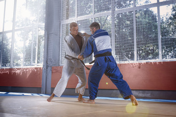 Two judo fighters showing technical skill while practicing martial arts in a fight club. The two fit men in uniform. fight, karate, training, arts, athlete, competition concept