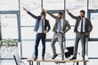 © LIGHTFIELD STUDIOS - three happy young businessmen dancing on table in office