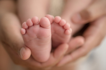 Feet of a newborn baby in the hands of parents. Happy Family oncept. Mum and Dad hug their baby's legs.