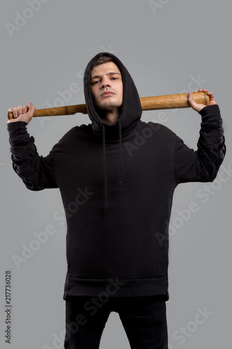 A young guy dressed in a black sweatshirt with baseball bat on grey  background in studio - Buy this stock photo and explore similar images at  Adobe Stock | Adobe Stock