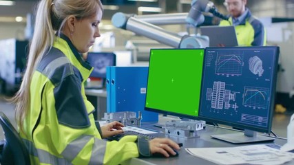Fototapete - At the Factory: Female Chief Engineer Works on the Green Mock-up Screen Personal Computer with Two Displays, Second Display Shows Graphics Blueprint for Engine.