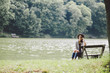 © Cavan Images - Portrait of woman sitting on bench at lakeshore in forest