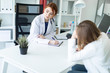 © Ivan Traimak - A beautiful young girl in a white robe is sitting at the desk in the office and communicating with the interlocutor. The girl makes notes in the sheet.