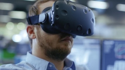 Fototapete - Portrait Shot of the Industrial Engineer Wearing Virtual Reality Headset and Gesturing with Controllers. In the Background Out of Focus Displays and Manufacturing Plant.