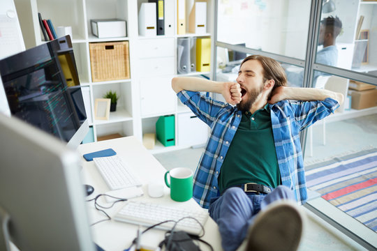 Young tired or bored software developer sitting in front of computer monitor and yawning