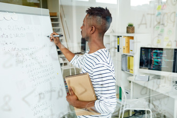 Wall Mural - young trainee with notepad writing down software codes on whiteboard in office