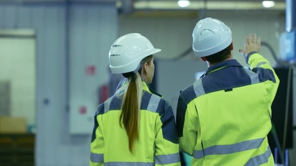 Aufkleber - Male Industrial Worker and Female Chief Mechanical Engineer in Walk Through Manufacturing Plant while Discuss Factory's New Project and Using Laptop. Facility Has Working Machinery.