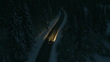 Aerial Shot Of Cars Driving Through A Snowy Forest At Night.