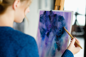 Poster - art painting hobby. creative leisure. girl drawing an abstract blue watercolor picture on easel in a workshop. talent inspiration creation and self expression concept.