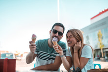 Good Looking Young Man Eating His Girlfriends Ice-cream While They Sitting Outdoors And Having Fun Times