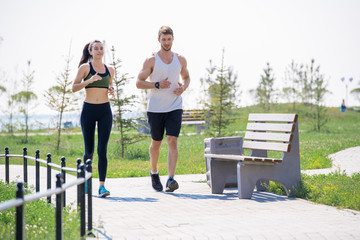 Full length portrait of modern young couple running together outdoors in park, copy space