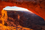 Fototapeta Zachód słońca - Cliff's-edge sandstone Mesa Arch framing an iconic sunrise view of the red rock canyon landscape below.