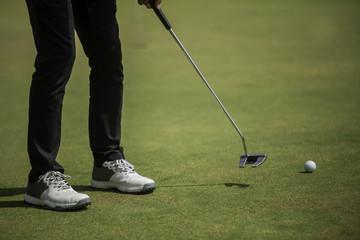 Wall Mural - Golf player at the putting green hitting ball into a hole