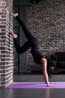© undrey - Beginning female yogi practicing yoga inversion poses standing on hands upside down leaning against wall in fitness club