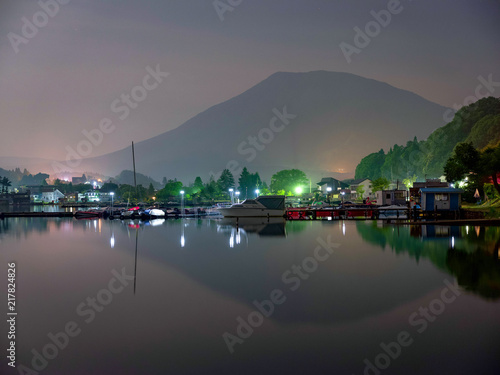 夜の湖畔にて、霞で山のシルェツトも掠れて、湖面には街灯りが上下対称的に写る。