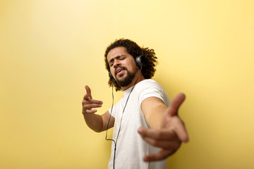 Wall Mural - A curly-headed tanned man wearing headphones is pointing at the camera with his eyes closed.