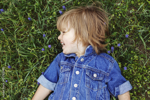 Cute Smiling Little Boy With Long Hair Lying On The Grass With