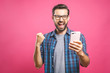 © denis_vermenko - I'm a winner! Happy man holding smartphone and celebrating his success over pink background.