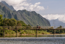 Lao Man In Scooter Runs Through A Wooden Bridge On The Nam Song River In Vang Vieng, Laos