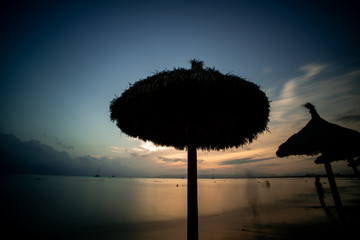 Wall Mural - Beach umbrella or parasol on a deserted tropical beach silhouetted against a beautiful bright yellow sunset or sunrise over the ocean