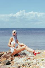 elegant woman in retro swimsuit holding ice cream and posing on rocky beach at sea