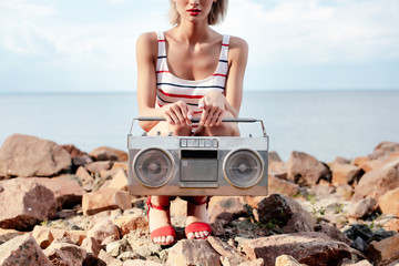 cropped view of girl posing with vintage boombox on rocky shore