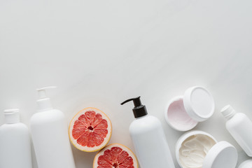 Wall Mural - flat lay with containers of lotion and pieces of grapefruit on white surface, beauty concept