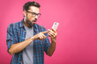 © denis_vermenko - Portrait of a surprised casual man looking at mobile phone isolated over pink background.