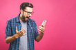 Young caucasian man angry, frustrated and furious with his phone, angry with customer service over pink background.
