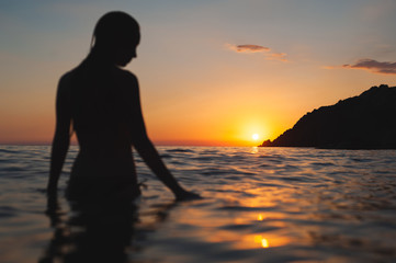 Wall Mural - wet woman sunset silhouette in water. Sea bathing at dawn