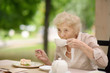 Beautiful senior lady with curly white hair drinking tea in outdoors cafe or restaurant