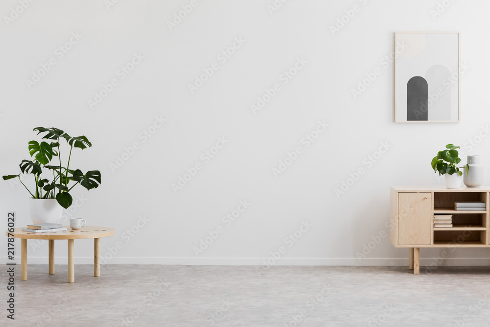 Empty space for your sofa in real photo of bright living room interior with fresh plants, simple poster and books on wooden cupboard - obrazy, fototapety, plakaty 