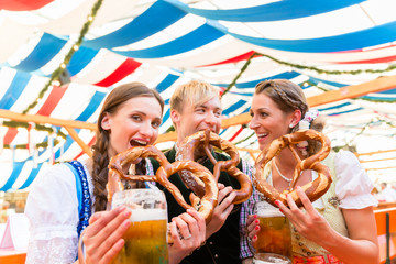 Three friends at the Regensburger Dult eat giant pretzels and drink beer in tent 