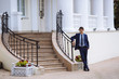 © romannoru - A man in a business dark suit is standing at the stairs on the street with his legs crossed and waiting for someone, he worries and smiles slightly.