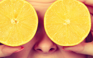 Woman holding fruit lemon half on eyes