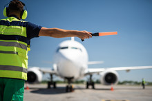 Important Signal. Back View Of Airport Worker Meeting Aircraft And Showing Right Position For Landing